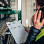 Female warehouse clerk using phone and looking at purchase order